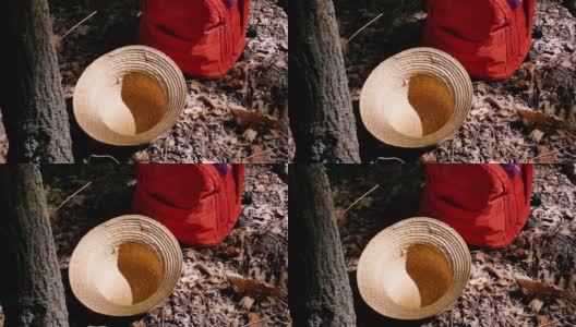 一顶草帽和一个背包躺在枯叶下的树旁。高清在线视频素材下载