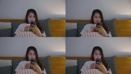 孤独的年轻亚洲女人使用智能手机和社交媒体盖着毯子在卧室高清在线视频素材下载