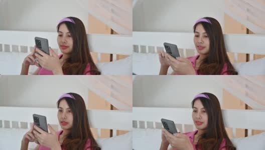 年轻的亚洲女人在酒店的床上使用和触摸智能手机高清在线视频素材下载