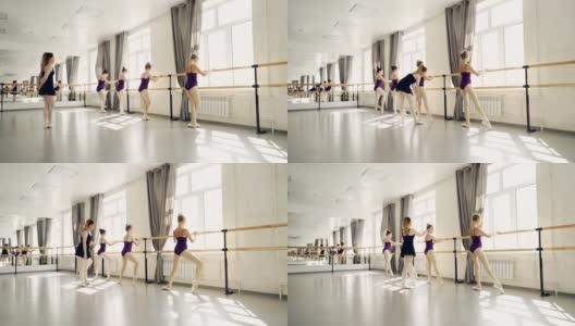 年轻的芭蕾舞演员在专业芭蕾舞演员严格的老师的指导下在芭蕾舞酒吧练习腿的姿势。灯光舞厅配有大镜子。高清在线视频素材下载