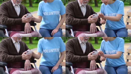 女志愿者教坐在轮椅上的残疾老人如何使用手机高清在线视频素材下载