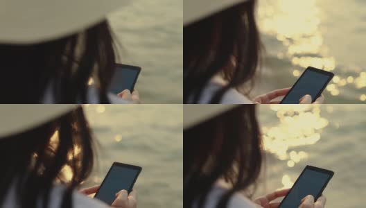 近距离的亚洲女人手打字智能手机上的信息，而站在海滩上的日落。生活方式旅游度假夏季概念。高清在线视频素材下载