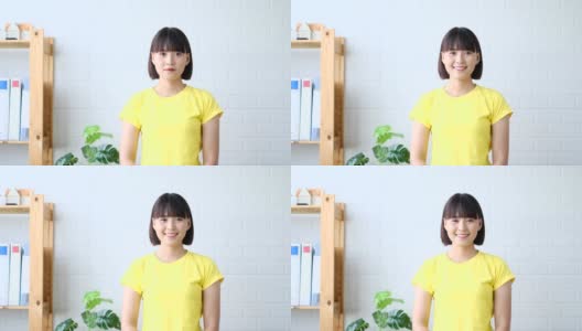 快乐的年轻亚洲妇女交叉双臂微笑，站在白色墙壁的背景。看着相机，她很兴奋高清在线视频素材下载
