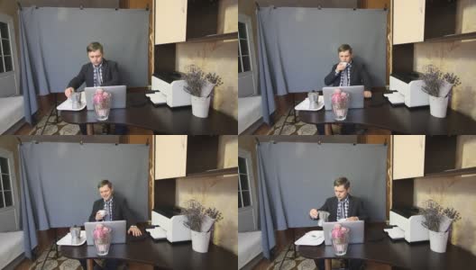 在视频通话中吃东西。一个穿着西装的男人正在通过视频通信交谈。在交流的时候，他会打手势，喝咖啡。旁边的托盘上放着一台咖啡机，里面放着咖啡。高清在线视频素材下载