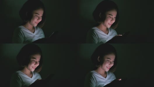 年轻的微笑女孩使用她的手机晚上躺在床上。高清在线视频素材下载