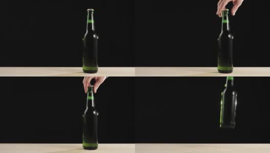新鲜的啤酒。Hand从黑色背景的木桌上拿起一个绿色的瓶子，里面装着美味的精酿啤酒。冰镇新鲜啤酒与水滴。准备饮料。广角镜头。4 k高清在线视频素材下载