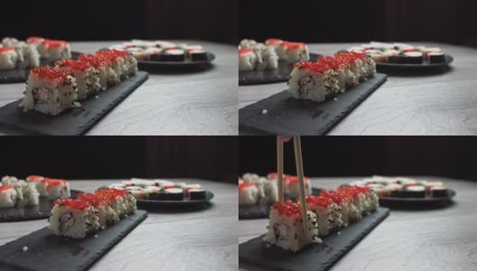女人用筷子拿食物。寿司卷日本食物旋转在黑色的背景。加州寿司卷配金枪鱼，蔬菜，飞鱼卵和鱼子酱近距离旋转。日本餐厅菜单。4 k生高清在线视频素材下载
