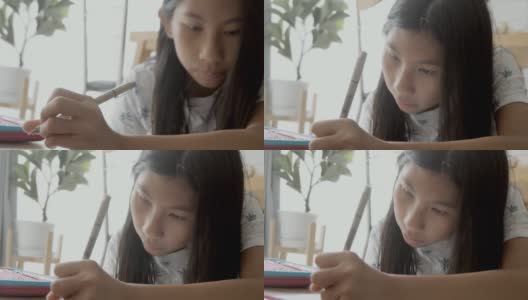 亚洲女孩一边做作业一边在家学习在线课程，社交距离的生活方式概念。高清在线视频素材下载