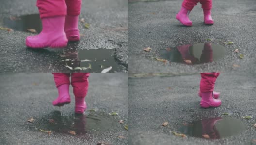快乐的小女孩跑过水坑，特写。可爱的小女孩在雨后穿着粉红色的胶靴走路。高清在线视频素材下载