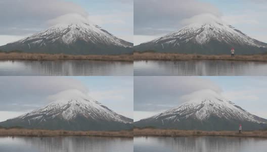 游客漫步在新西兰北岛的塔拉纳基火山，与山和登山者在湖中的倒影在一起。新西兰被高清在线视频素材下载