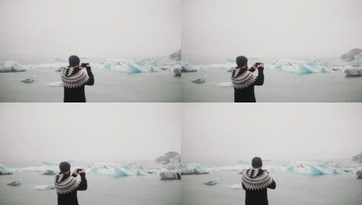 年轻的旅行男子站在冰岛的Jokulsalon冰礁湖，用智能手机拍摄冰川的背影高清在线视频素材下载