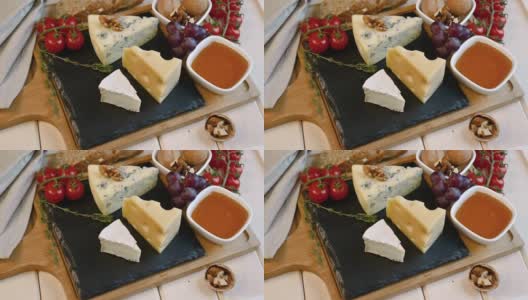 手把奶酪刀放在桌子上，上面放着奶酪，坚果，蜂蜜，葡萄和西红柿，放在木板和托盘上。奶酪盘配刀。高清在线视频素材下载