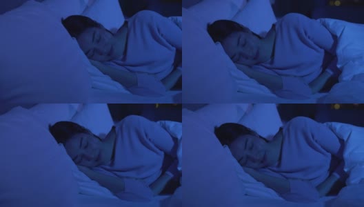 安静漂亮的年轻女人晚上闭着眼睛睡在她舒适的床上，盖着毯子。高清在线视频素材下载