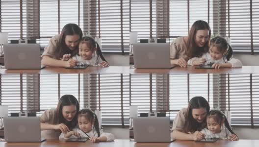 亚洲母亲教女儿做家庭作业后，从学校在家里，母亲工作使用笔记本电脑数字技术。高清在线视频素材下载