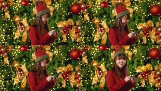 穿着红色毛衣在圣诞树前玩手机的成熟女人高清在线视频素材下载