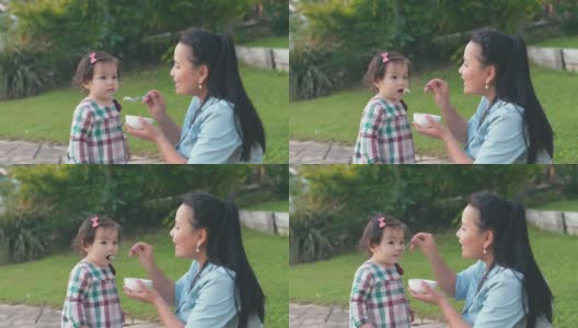 亚洲母亲在前院喂养她的混合蹒跚学步的女儿，家庭生活理念高清在线视频素材下载
