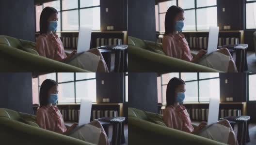 亚洲妇女戴着口罩，坐在沙发上使用笔记本电脑在现代办公室高清在线视频素材下载