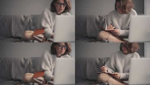 一个年轻的女人看着笔记本电脑的屏幕，在她的笔记本上做笔记高清在线视频素材下载