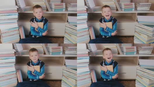7岁的小男孩抱着书，对着镜头微笑，坐在书中。特写镜头。高清在线视频素材下载