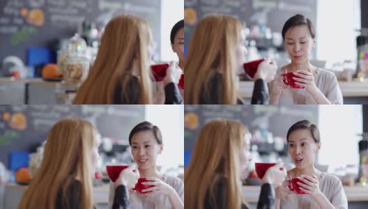 右图是两个年轻女人在咖啡馆喝茶或喝咖啡聊天的画面。亚洲女性讲述故事分散的白人朋友高清在线视频素材下载