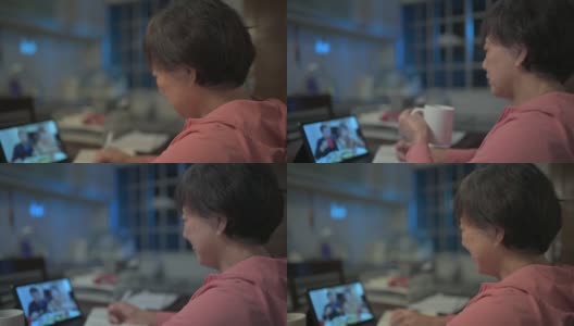 一名亚洲华裔老妇人晚上在厨房用数字平板电脑与她的儿子和儿媳进行视频通话高清在线视频素材下载