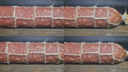 在细节。多莉拍摄了一根意大利腊肠，木桌上系着一根绳子，背景是黑色。用光线绘画和对比。高清在线视频素材下载