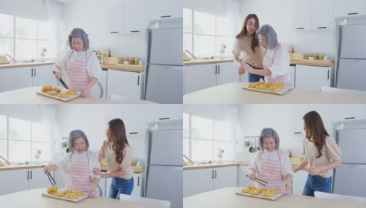 亚洲可爱的家庭，年轻的女儿看着老妈妈在厨房做饭。美丽的女性享受打发闲暇时光，抱着年迈的妈妈在家里的餐桌上烤牛角面包。活动的关系高清在线视频素材下载
