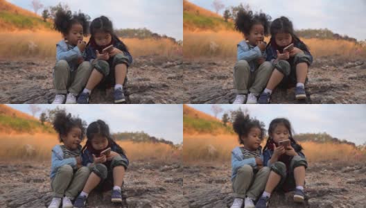 不同的孩子朋友非洲裔美国人和亚洲女孩一起使用智能手机在自然的山上与阳光。一群孩子在花园公园用手机玩互联网。高清在线视频素材下载