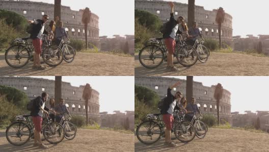 三个快乐的年轻朋友游客与自行车和背包在罗马斗牛场挥手，在山上的日落与树木的慢镜头娱乐高清在线视频素材下载
