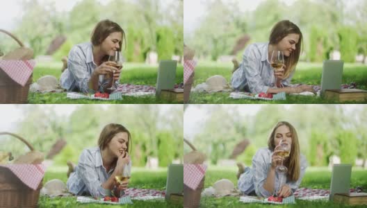 女人躺在毯子上，喝着酒，用笔记本电脑野餐高清在线视频素材下载