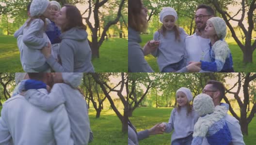 幸福的一家人在草地上拥抱。父母和他们的两个女儿在公园的草坪上拥抱。花期果园。高清在线视频素材下载