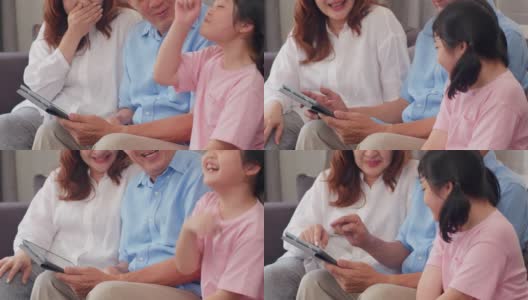 亚洲的祖父母和孙女在家里使用平板电脑。大四的中国，爷爷奶奶开心的花家人放松与年轻的女孩查看社交媒体，躺在客厅的沙发上。缓慢的运动。高清在线视频素材下载