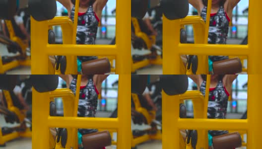 前方的亚洲年轻女性正在健身房锻炼和训练，通过机器举重来锻炼肌肉(背部和二头肌)，锻炼以提高力量，身体健康和牢固。高清在线视频素材下载
