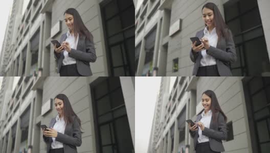 视频缓慢。亚洲女人，漂亮的女商人，白人，穿着黑色西装，在用智能手机聊天。在城市街道的一边高清在线视频素材下载