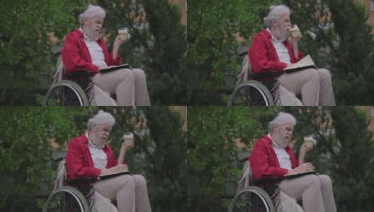 留着大胡子的白人残疾老人喝着卡布奇诺在户外用笔写日记。残疾的老年男性退休人员在后院的花园里喝咖啡，用慢动作书写思想。高清在线视频素材下载