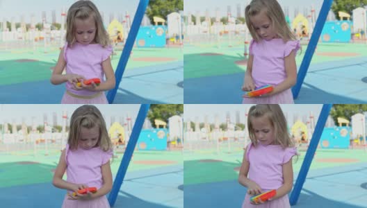 一个穿着粉红色裙子的女孩在操场的背景上玩起了小游戏。孩子热衷于彩虹抗压力。孩子的硅胶玩具高清在线视频素材下载