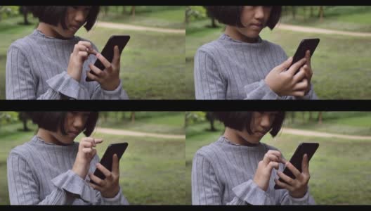 4 k。儿童亚洲女孩看着使用移动智能手机在绿色公园户外。高清在线视频素材下载
