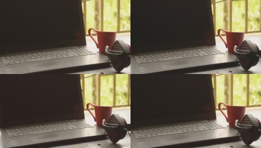 带麦克风的耳机放在靠近笔记本电脑的地方，在早晨的阳光照射下。红杯咖啡在远处。呆在家里，在家工作，远程工作，业务连续性背景。高清在线视频素材下载