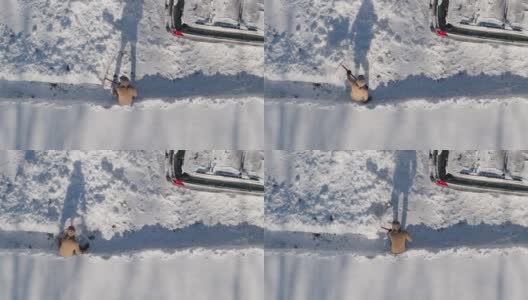 一名成年男子在一场冬季降雪后用铲子清理车道上的积雪。鸟瞰无人机正上方的慢动作视频。高清在线视频素材下载