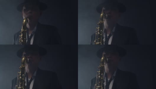优雅的男子在一顶帽子和正式的西装演奏萨克斯在深灰色的背景在烟雾演播室。音乐家在黑暗中吹萨克斯管高清在线视频素材下载