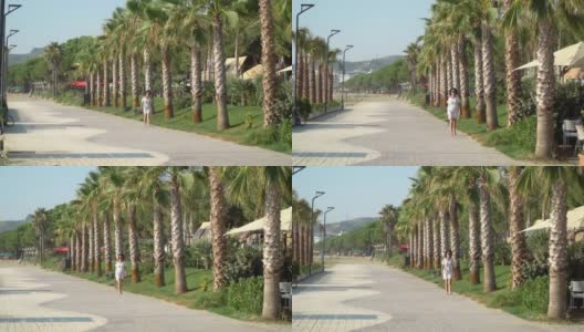 在暑假里，穿着白色衣服的女人在散步道上的棕榈树间漫步高清在线视频素材下载