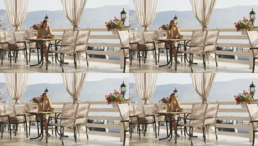 年轻漂亮的女人坐在咖啡馆里欣赏海湾的美景。高清在线视频素材下载