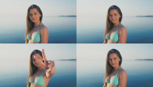 海滩上快乐的年轻女子。女游客穿着比基尼在假期对着镜头做和平手势高清在线视频素材下载