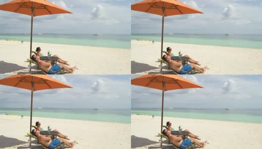 一男一女在海边的日光浴床上晒太阳高清在线视频素材下载