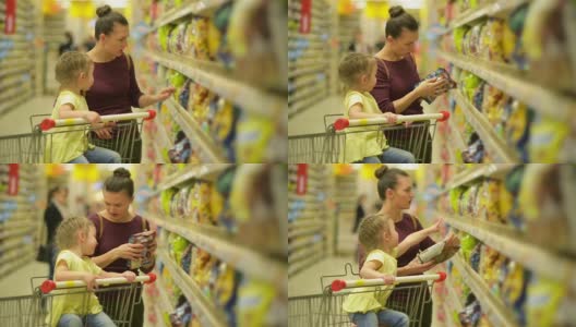 母亲和女儿在超市购物。他们在买早餐片。坐在超市购物车里的女儿高清在线视频素材下载