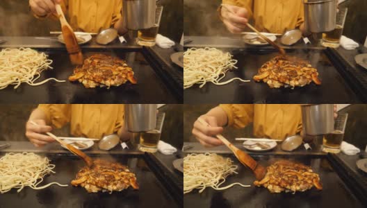 在日式餐厅里，一名年轻女子正在往御好烧里加酱高清在线视频素材下载