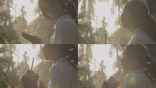 年轻的亚洲女人喝椰子水在日落，阳光周末公园高清在线视频素材下载