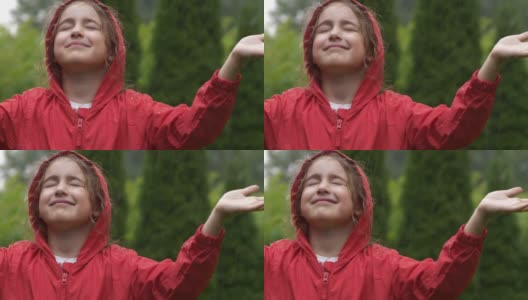 快乐的小女孩在雨中微笑。孩子热爱自然，幸福自由。孩子玩雨滴雨。孩子在下雨的夏天在户外玩耍。穿红雨衣的女孩欣赏秋日降雨。高清在线视频素材下载