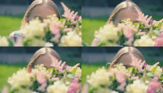 年轻的女演员对着镜头低头凝望，透过鲜花的装饰，在绿茵茵的草坪上进行接待装饰高清在线视频素材下载