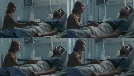 在医院里，忧心忡忡的妻子坐在她生病的丈夫的床边。她握着他的手，和他说话，希望他能痊愈。高清在线视频素材下载